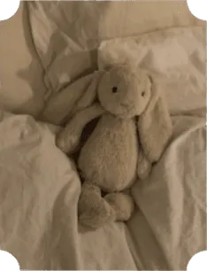 Doudou lapin en peluche crème posé sur des draps